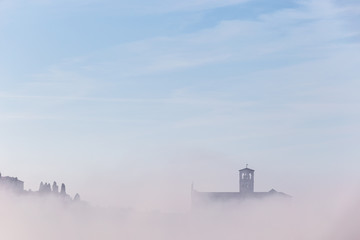 A view of a silhouette of St.Francis church in Assisi in the middle of mist beneath a blue sky with...