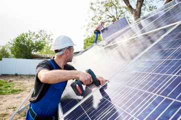 Engineer technician connecting solar photo voltaic panel using screwdriver with team of workers on metal platform. Stand-alone solar system installation, efficiency and professionalism concept.