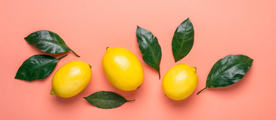 border of ripe lemons and leaves on a living coral background. Banner format