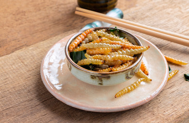 Bamboo edible worm insects crispy or Bamboo Caterpillar in a ceramic bowl on a wood table. The concept of protein food sources from insects. It is a good source of protein, vitamin, and fiber.