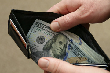 A large stack of modern U.S. $100 bills is displayed in a black wallet.