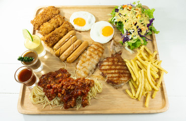 Fried fish, chicken, Pork steak , Roasted sausage and Spaghetti bolognese with tomato sauce in a dish on a white wood floor table. Food background concept. Top view with copy space for your text..