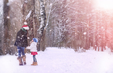 A winter fairy tale, a young mother and her daughter ride a sled in the forest. A girl on a sled with gifts on the eve of the new year in the park.
