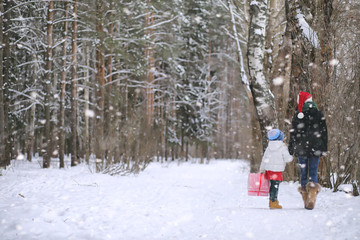 Fototapeta na wymiar A winter fairy tale, a young mother and her daughter ride a sled in the forest. A girl on a sled with gifts on the eve of the new year in the park.