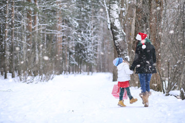 A winter fairy tale, a young mother and her daughter ride a sled in the forest. A girl on a sled with gifts on the eve of the new year in the park.