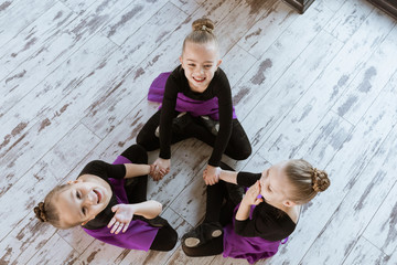 Naklejka premium Top view of kids in black uniform and skirt sitting on floor at dance studio after dancing modern ballet, embracing and smiling together in the class.