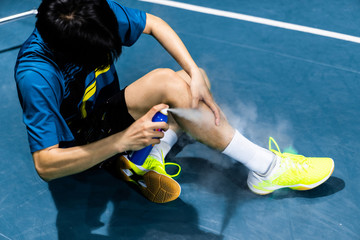 Asian badminton player is injured in the leg, he is cramping and using a spray