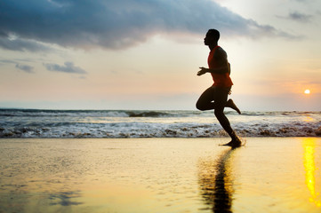 Fototapeta na wymiar silhouette of young attractive fit athletic and strong black afro American man running at sunset beach training hard and sprinting on sea water runner workout
