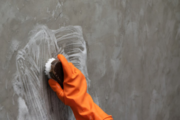 Woman's hand wearing orange rubber gloves is used to convert scrub cleaning on the concrete wall.