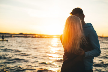 Silhouette of couple in love on the pier, sunset time, water bac