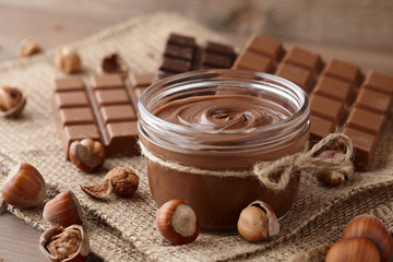 Chocolate spread or nougat cream with hazelnuts in glass jar on wooden background