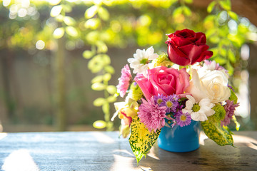 A vase full of assorted colourful flowers on wooden table with sunlight in the morning, outside at...