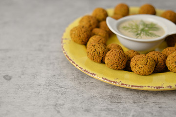 Baked chickpea falafel balls on yellow plate on grey background , healthy and vegan food with tahini deep , traditional Mediterranean , top view , flat lay with copy space  