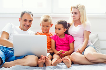 Loving family looking at a laptop lying down on bed at home