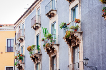 Fototapeta na wymiar Balcony with flowerpots and house plants in a historic building in Catania, traditional architecture of Sicily, Italy.
