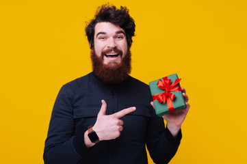 Photo of  happy bearded man with curly hair, pointing to small gift box