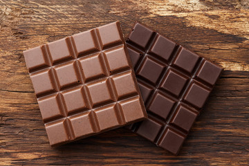 Milk and dark square shape chocolate bars on textured brown wooden background, top view