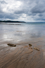 A cloudy and threatening sky is reflected on the wet sand of a beach in northern Brittany at low tide on a rainy day