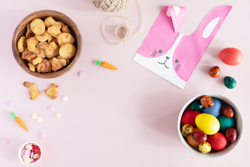 Flat lay of arrangement decorations for Happy Easter holiday. Springtime background. Top view of colorful eggs, bunny bag, cookies on pastel pink table desk.