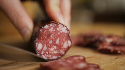 Man cuts into thin slices fatty sausage. Shooting closeup. Chef cutting salami with a knife on a wood board close up.