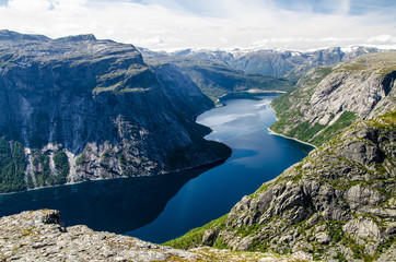 Spectacular view of a blue lake 700 meters lower under the Trolltunga rock and interesting sky with few clouds