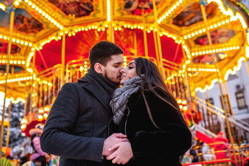 young couple standing near the bright carousel, cuddles and kisses,concept of joint rest