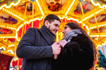 young couple standing near the bright carousel, cuddles and kisses,concept of joint rest