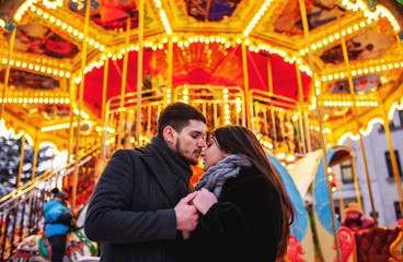 young couple standing near the bright carousel, cuddles and kisses,concept of joint rest