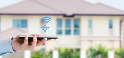 Hand using smart phone with smart home control icon over blur house background, smart home control...