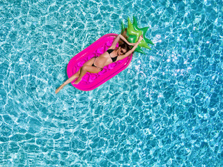 Sportliche, junge Frau im Bikini entspannt auf einer Luftmatratze im Pool an einem heißem Sommertag