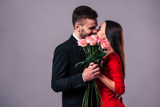Close up photo of beautiful young romantic couple while they kissing behind the bouquet of roses in hands. St Valentine's day.