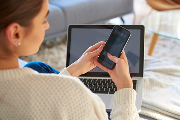 Woman text messaging on cell phone while sitting on sofa at home