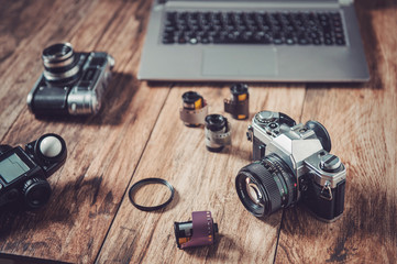 Analog camera, film rolls and vintage photography accessories along with modern equipment and laptop.