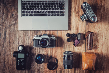 Analog camera, film rolls and vintage photography accessories along with modern equipment and laptop.