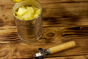 Opened tin can of pineapple pieces and can opener on wooden table