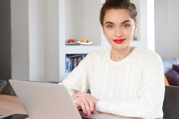 Smiling young attractive woman with laptop sitting at home and studying