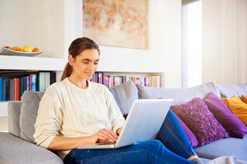 Fototapeta premium Beautiful young woman with her laptop sitting on couch