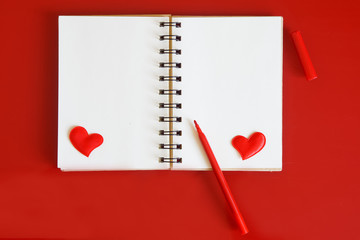 Notebook with hearts and pencil on a red background. Preparation for congratulations on Valentines Day. Template