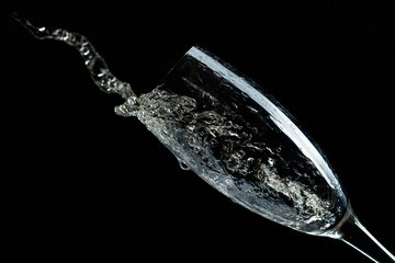 Glass of splashing champagne isolated on black.