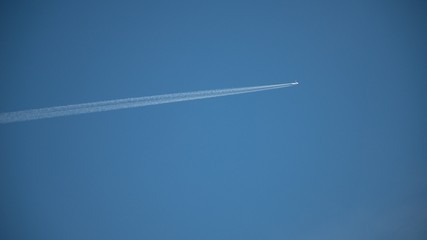 Plane flying on a blue sky, condensation line.