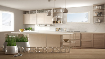 Wooden table, desk or shelf with potted grass plant, house keys and 3D letters making the words interior design, over blurred modern kitchen, project concept copy space background