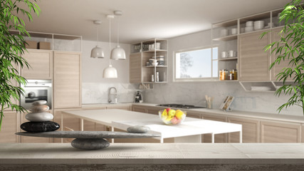 Wooden vintage table or shelf with stone balance, over blurred modern white kitchen with wooden details and parquet floor, feng shui, zen concept architecture interior design