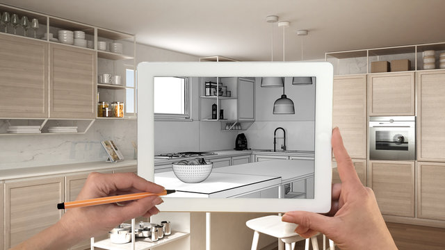 Hands holding and drawing on tablet showing modern white kitchen with wooden details CAD sketch. Real finished interior in the background, architecture design presentation