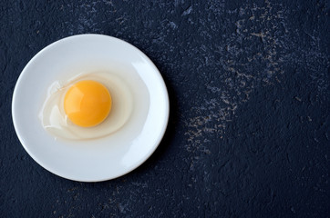 Raw egg guinea fowl in a white plate on a blue background