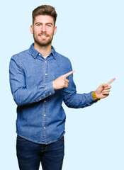 Young handsome blond man wearing casual denim shirt smiling and looking at the camera pointing with two hands and fingers to the side.