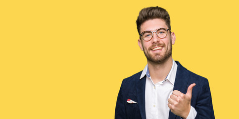 Young handsome business man wearing glasses doing happy thumbs up gesture with hand. Approving expression looking at the camera with showing success.