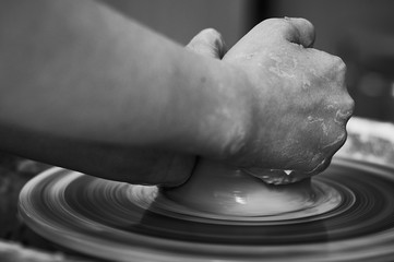 Black and white A man teaches a girl to make clay products on a potter's wheel. Hands close up.