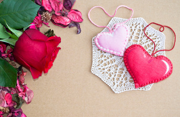 red rose on a background of dried rose petals and textile hearts on knitted cloth