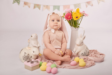 Cute funny baby with bunny ears and colorful Easter eggs and rabbits. Easter Baby. Greeting Easter card template. Girl baby in suit of rabbit for Easter. 