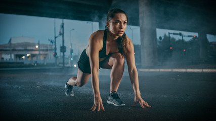 Beautiful Strong Fitness Girl in Black Athletic Top and Shorts Ready for Sprinting. She is Training in an Urban Environment Under a Bridge with Cars in the Background.